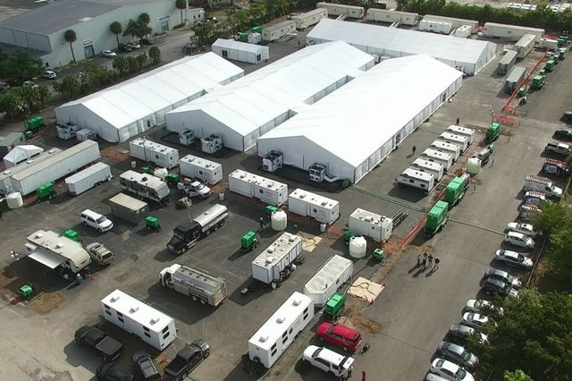 Several large white tents surrounded by large trucks